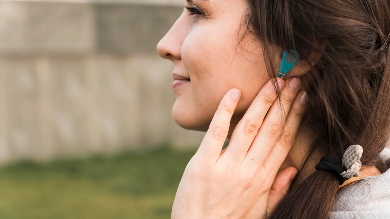 Audífonos y vida diaria: deporte, natación, sueño y viajes 1 Mujer en ropa deportiva con audífono retroauricular al aire libre, ejemplo de que audífonos y deporte son compatibles